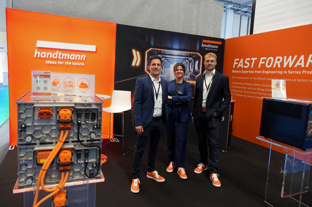 Drei Mitarbeitende von Handtmann Systemtechnik am neu gestalteten Messestand mit FAST FORWARD-Key-Visual und ausgestellten Batteriesystemen.