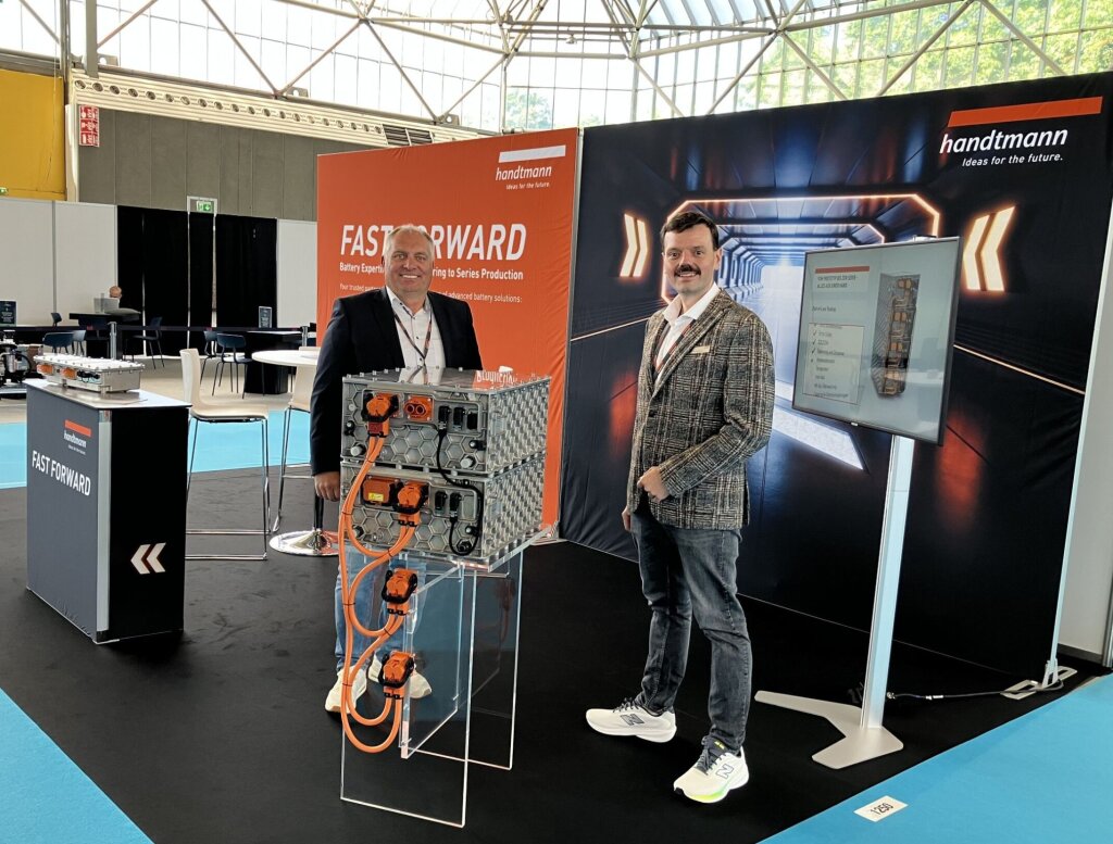 Zwei Mitarbeiter von Handtmann Systemtechnik am FAST FORWARD-Messestand mit ausgestellten Batteriesystemen und dem von SYNBRAND entwickelten Key Visual.