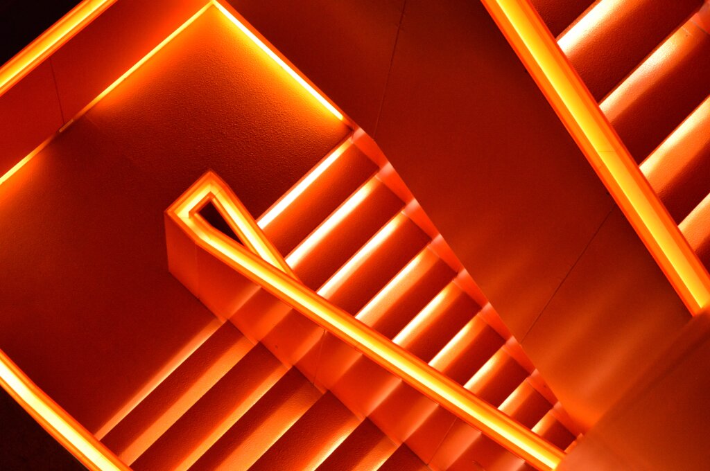 Geometrisch angeordnete Treppen mit orange leuchtenden Stufen und Gel&auml;ndern aus der Vogelperspektive.