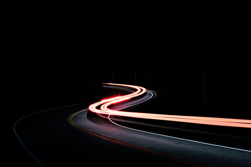 Rote Lichtspuren eines fahrenden Autos auf einer kurvenreichen Stra&szlig;e bei Nacht.